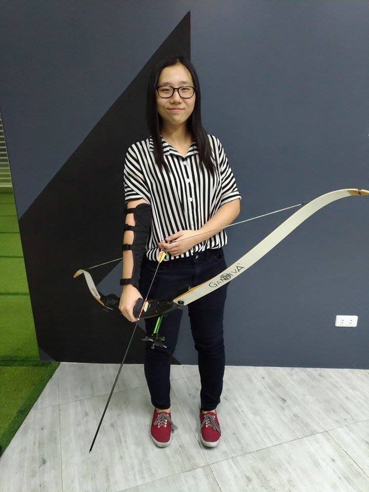 Archer posing with Gandiva bow in front of Arrowland branding wall